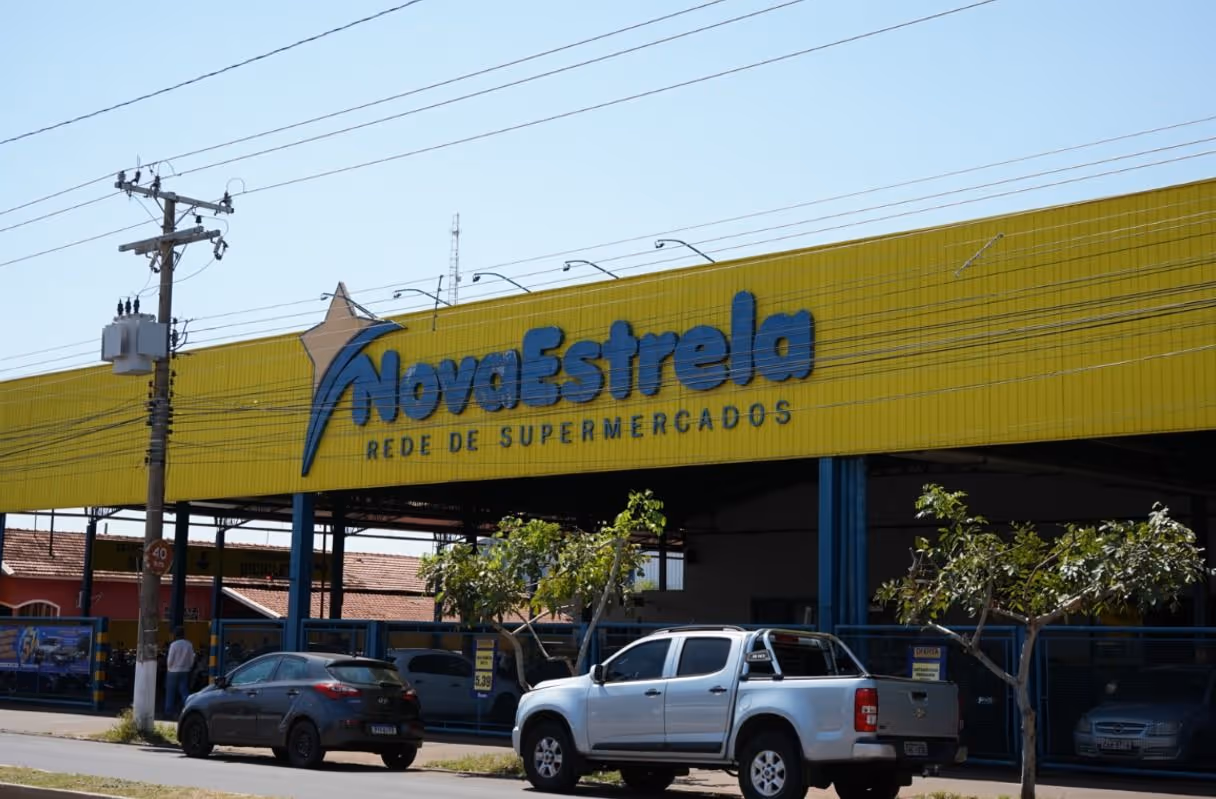 Fachada amarela do supermercado Nova Estrela com carros estacionados na frente.